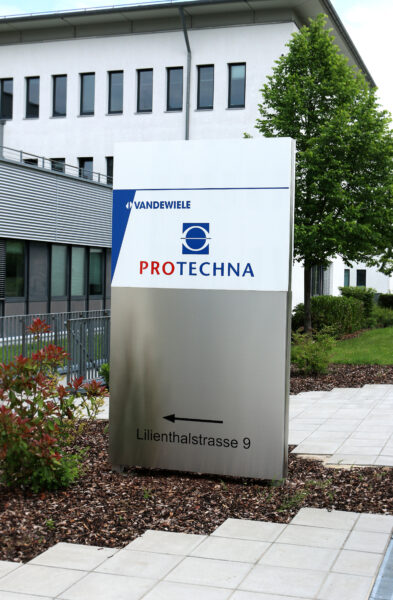 Firmenschild von PROTECHNA mit Logo und Adresse an einem modernen Gebäude.
